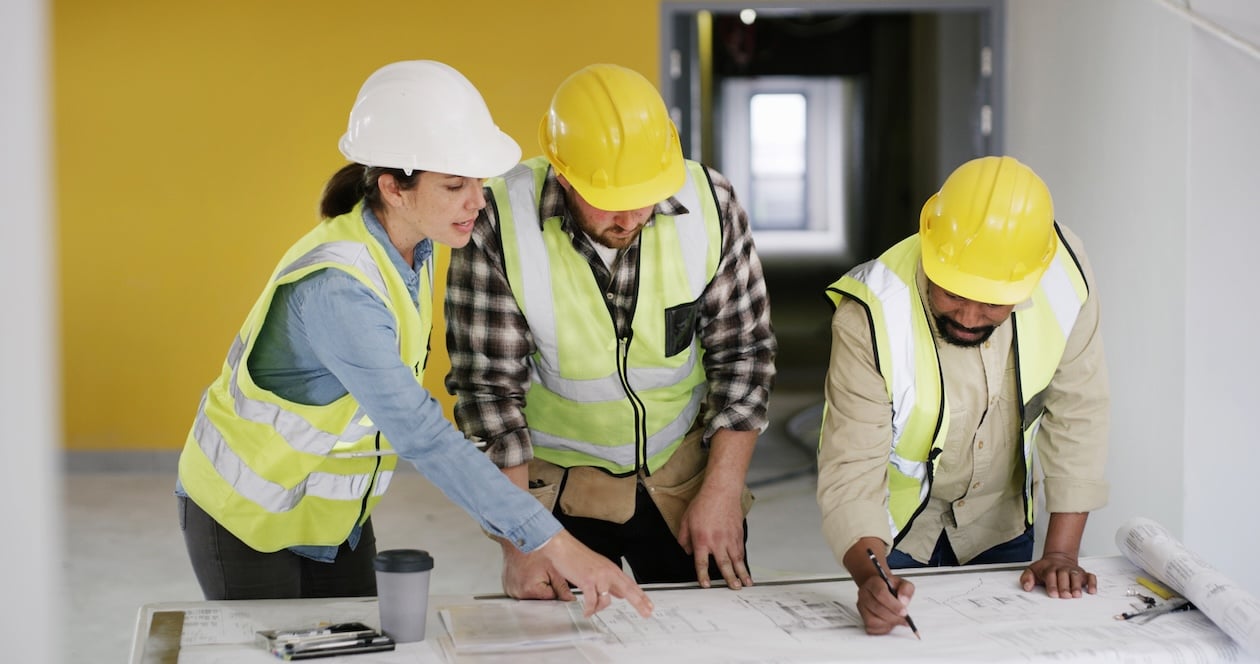 Team of architects and contractors reviewing floor plans and blueprints during a project planning meeting, collaborating on building design and layout decisions.