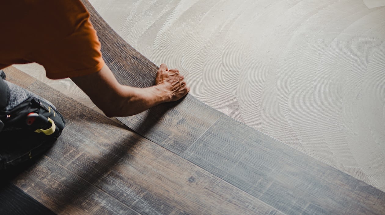 Worker installing vinyl tile flooring using the glue-down method during a professional flooring job.