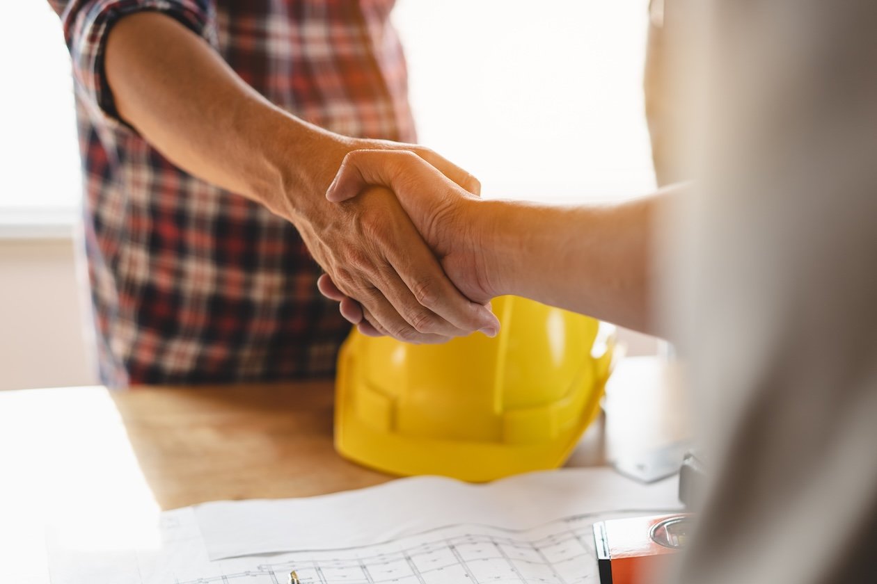 Flooring contractor and client finalize a renovation agreement with a handshake after reviewing plans.