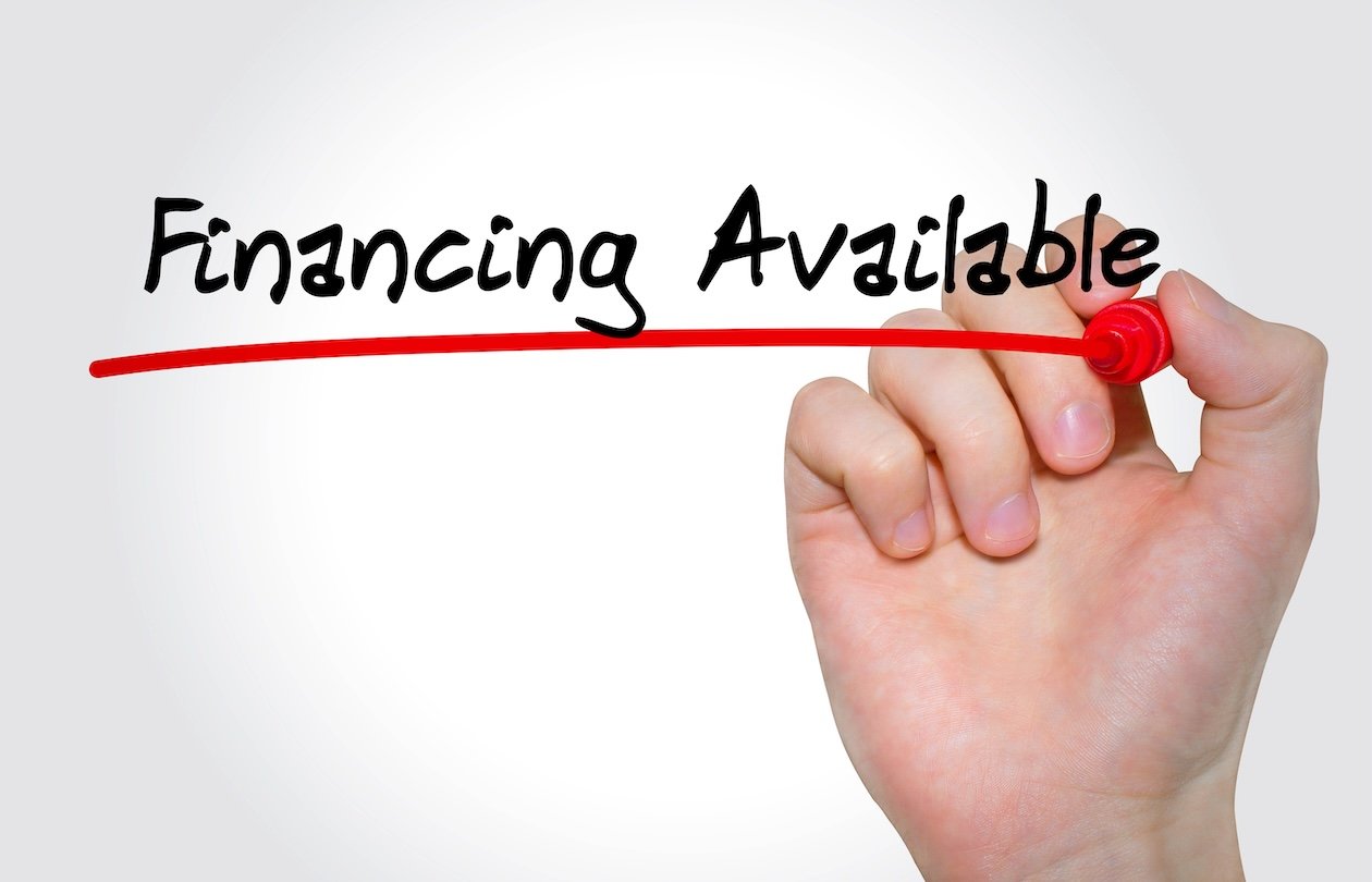Hand writing “Financing Available” with a black marker on a transparent surface, representing payment options or consumer financing for purchases.