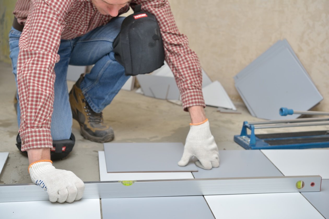 installing-ceramic-tiles-on-a-Installer laying ceramic floor tiles while wearing knee pads and gloves for safety.