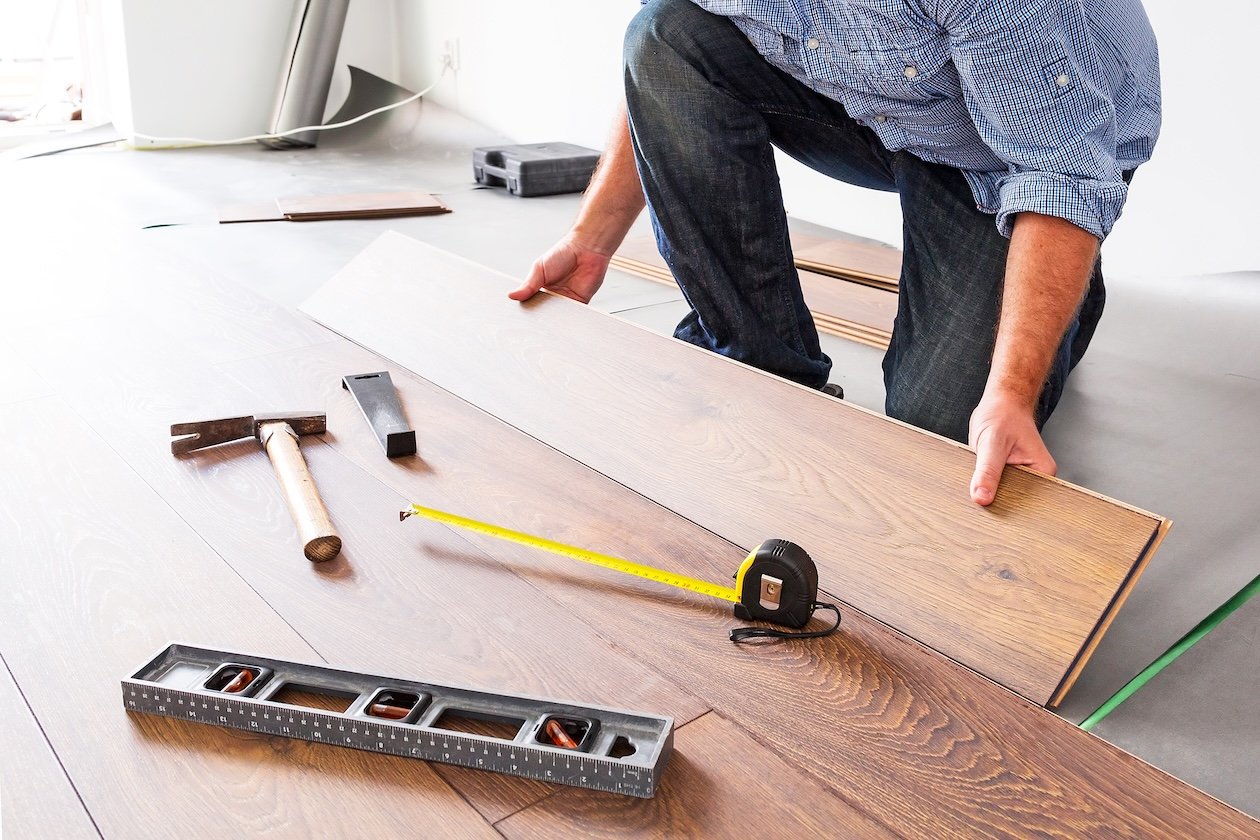 Installer laying laminated wooden flooring, aligning planks during a professional installation.