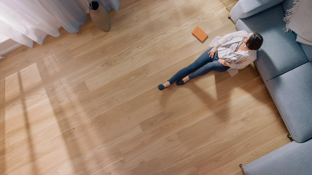 Top-view of a woman sitting on hardwood flooring in a modern living room with a cozy interior.