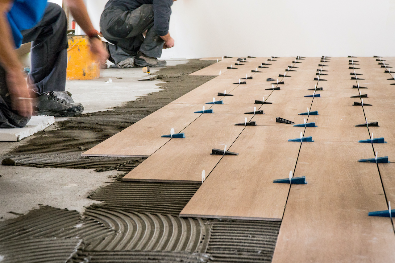 Construction workers laying tile over concrete floor using tile levelers.