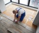 Flooring contractor in blue overalls installing a floor.