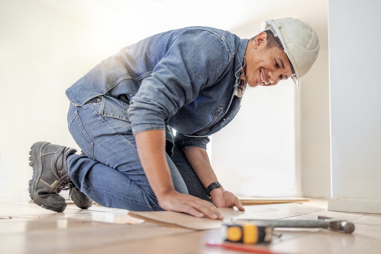 Flooring professional installing a floor with hardhat on.