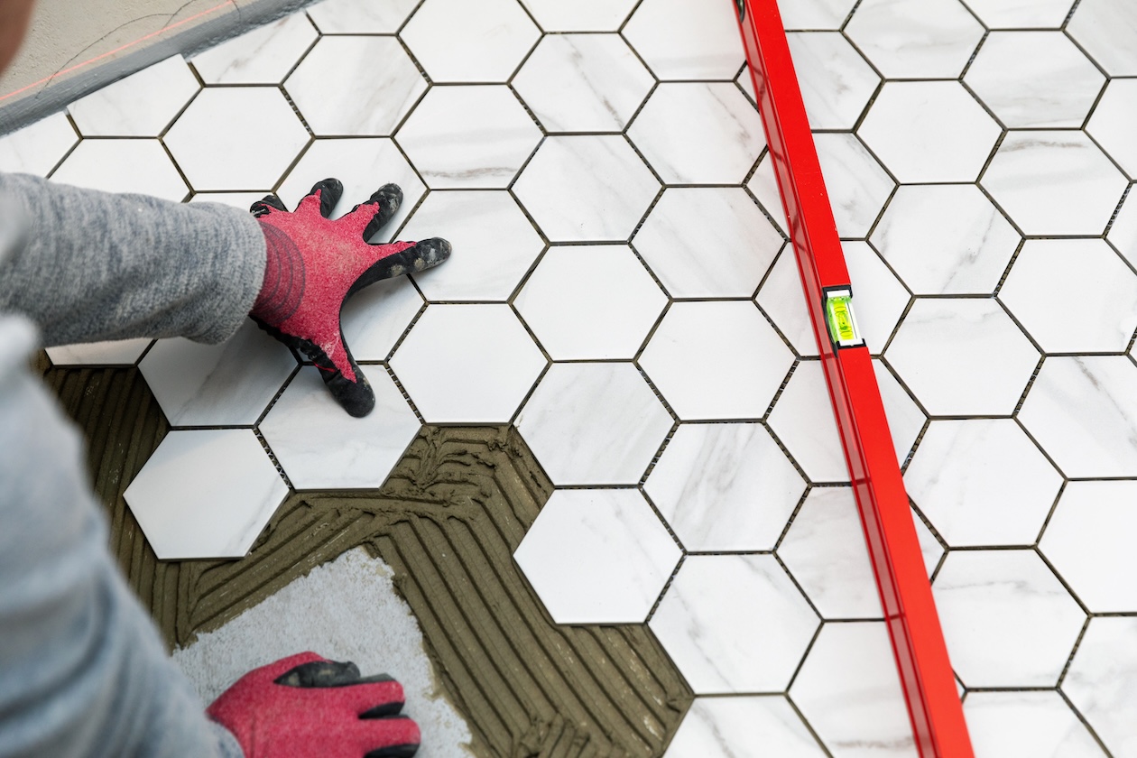 Contractor laying marble hexagon floor tiles in a bathroom during flooring installation.
