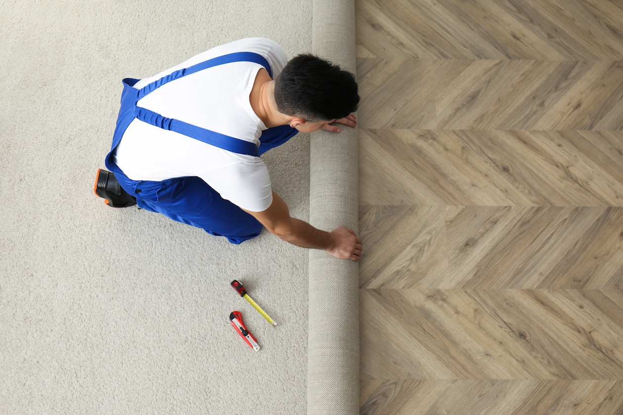 Worker unrolling new carpet indoors, top view of flooring installation process.